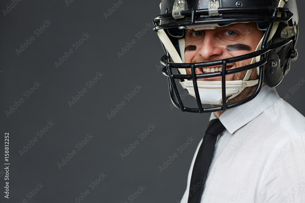 Closeup portrait of confident middle aged businessman with army paint on his face wearing helmet and smiling at camera against grey background, copy space to the left
