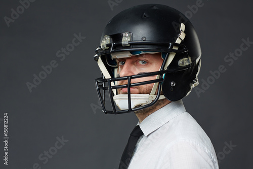 Closeup portrait of determined middle aged manager with army paint on his face wearing helmet and looking at camera against grey background