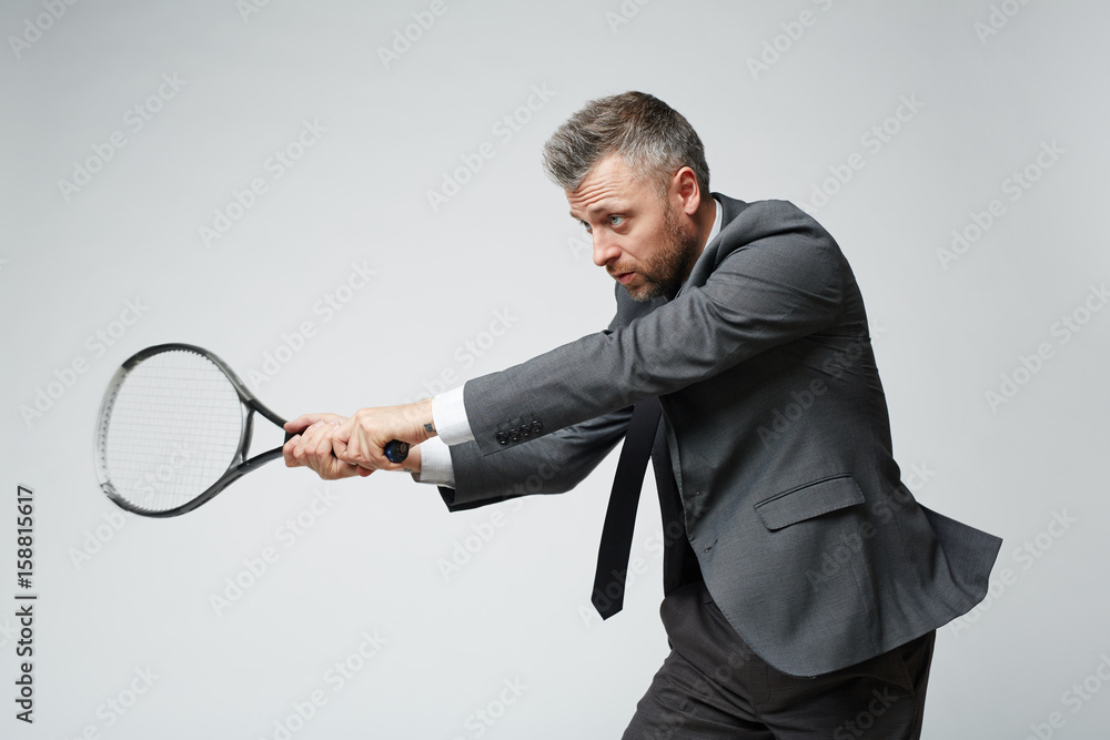 Waist up portrait of confident middle aged businessman countering tennis ball against grey background Waist up portrait of confident middle aged businessman countering tennis ball against grey background
