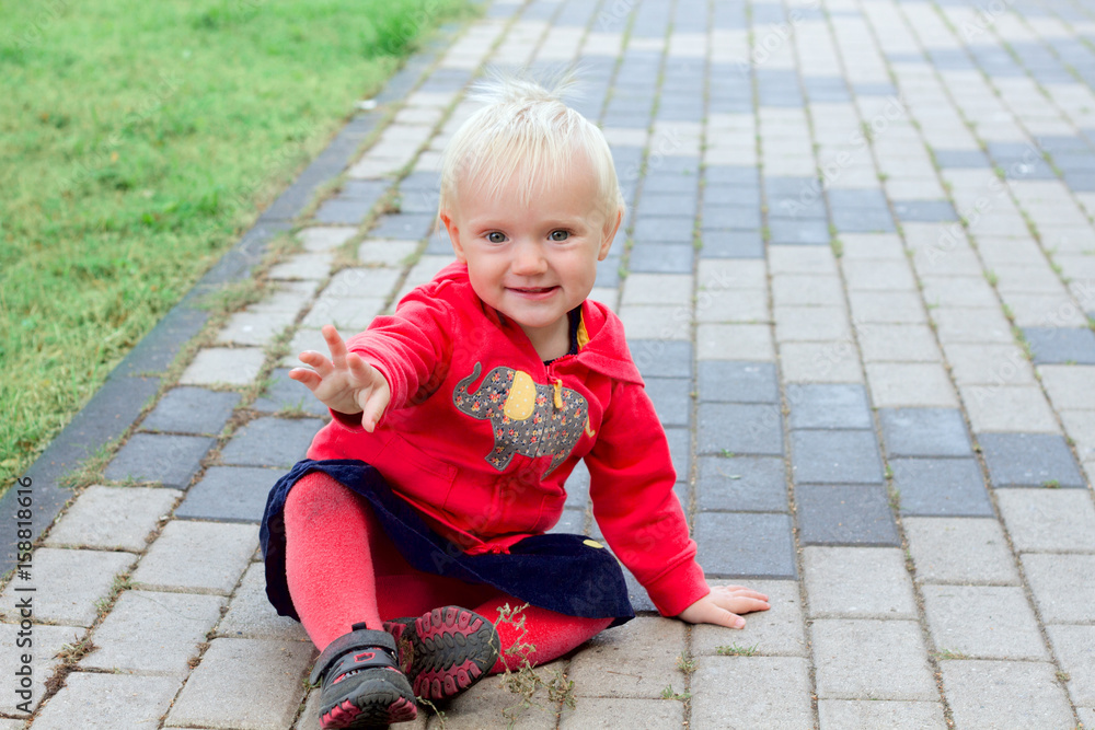 Cute blond baby sitting on the ground in the park Cute blond baby sitting on the ground in the park