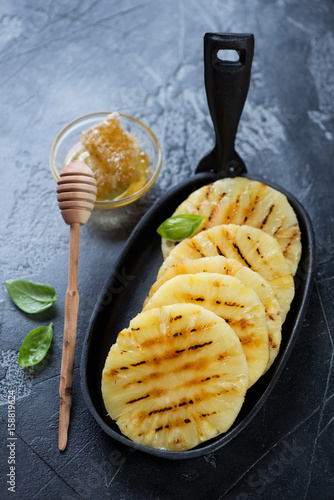 Grilled pineapple slices with addition of honey in a black cast-iron frying pan, studio shot