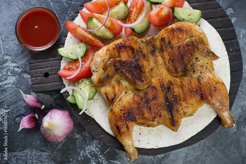 Above view of roasted chicken tapaka served on tortilla bread with fresh vegetables, studio shot photo