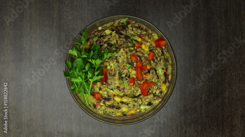 Black Bean and Avocado Dip in a Glass Bowl on Wooden Background. With Bell Pepper, Corn and Parsley.