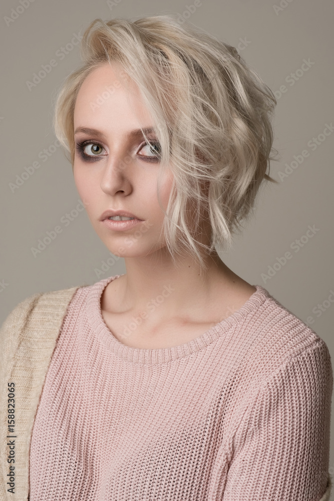 Portrait of girl of blonde with dark eye makeup and short hair, thrown on one side, light pink sweater on a light background Stock Photo | Adobe Stock Portrait of girl of blonde with dark eye makeup and short hair, thrown on one side, light pink sweater on a light background Stock Photo | Adobe Stock