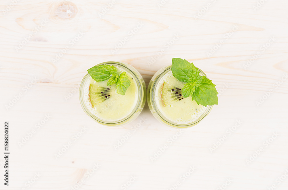Freshly blended green kiwi fruit smoothie in glass jars with straw, mint leaf, top view. White wooden board background, copy space. Freshly blended green kiwi fruit smoothie in glass jars with straw, mint leaf, top view. White wooden board background, copy space.