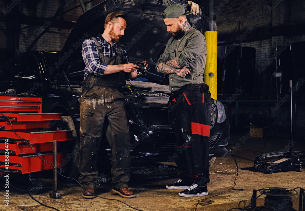 Two bearded mechanics inspecting car's engine parts. Two bearded mechanics inspecting car's engine parts.
