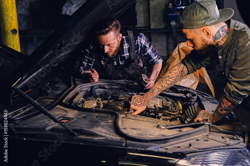 Two mechanics fixing car's engine in a garage.