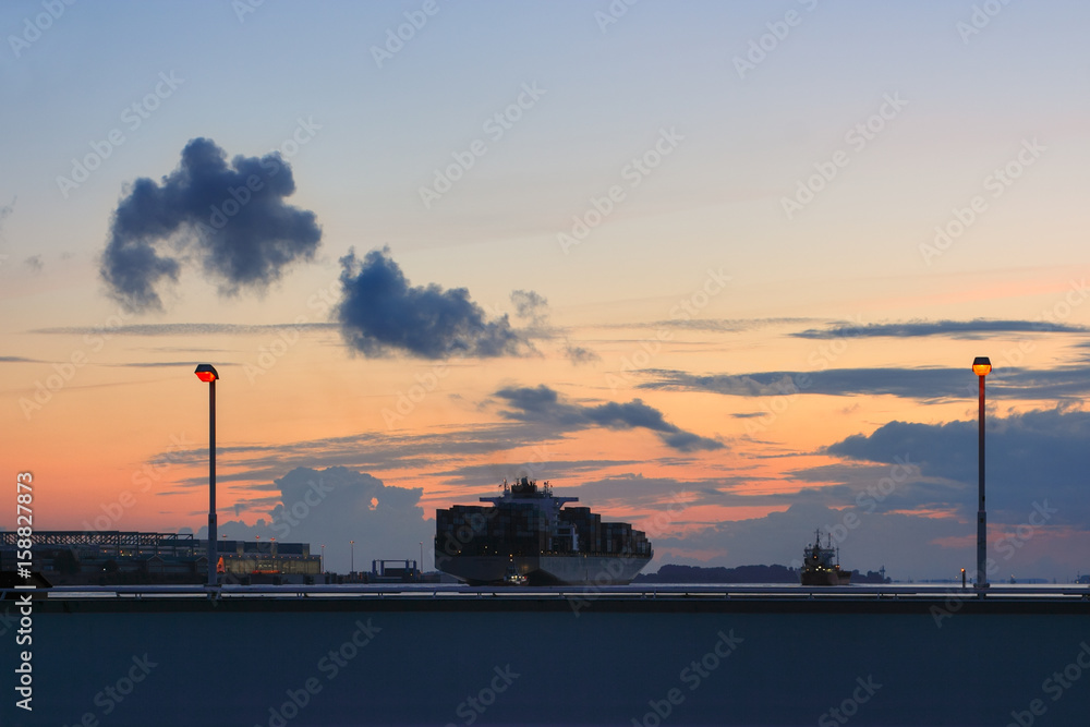 Shipping on the Elba river in twilight. Cargo ship and indastrial premises of the Airbus plant in Hamburg Finkenwerder.