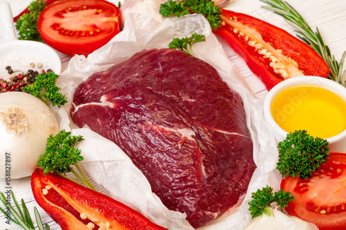 Beef meat with herbs and spices. Raw beef fillet preparation with oil, rosemary, garlic and fresh seasoning on white paper, close up