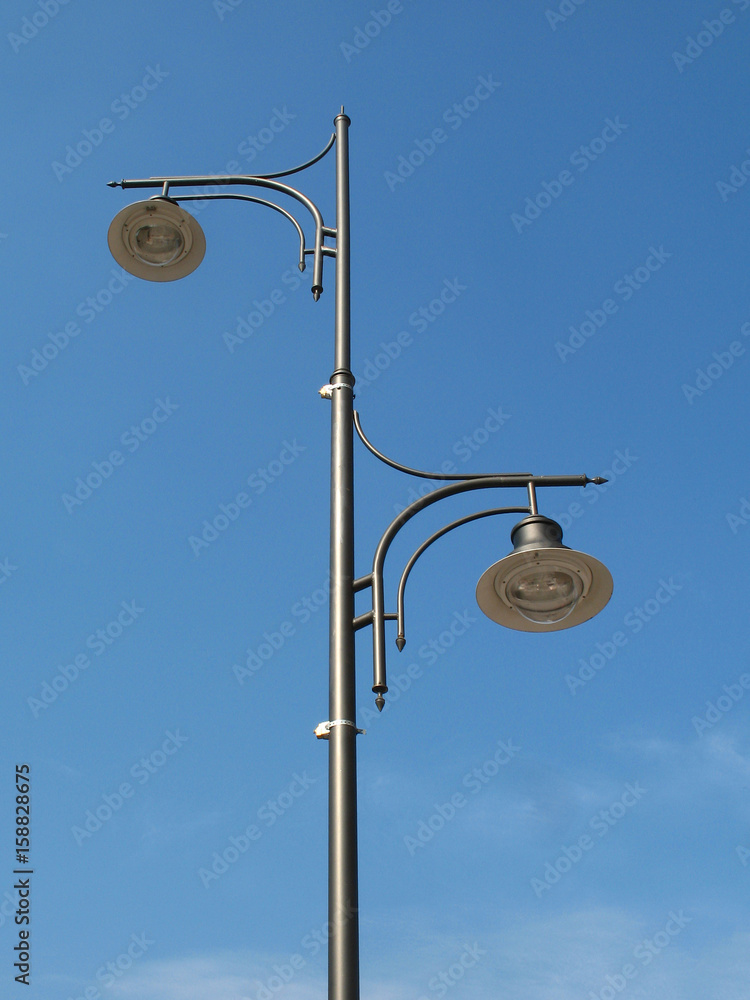 Two street lamps on lamppost against blue sky Two street lamps on lamppost against blue sky