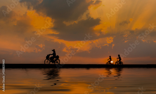 Silhouette,three children cycling on a sunset bike and shining on the beautiful water.