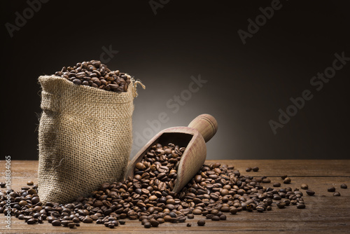 bunch of coffee beans with burlap sack and wooden scoop on table.