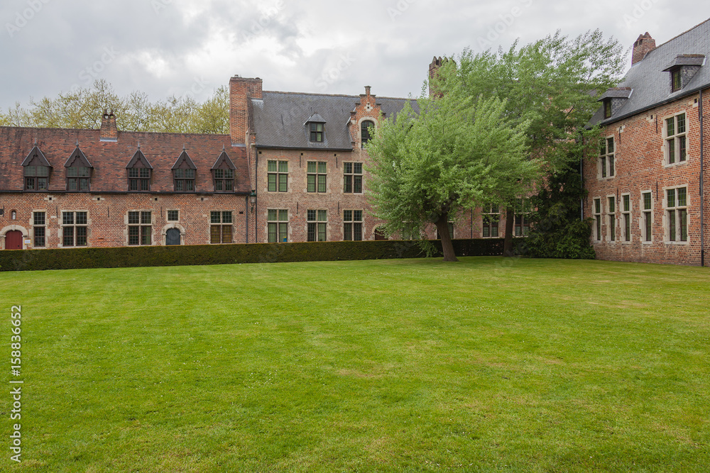 View of famous Grand Beguinage of Leuven with green lawn in foreground in spring cloudy day, Belgium