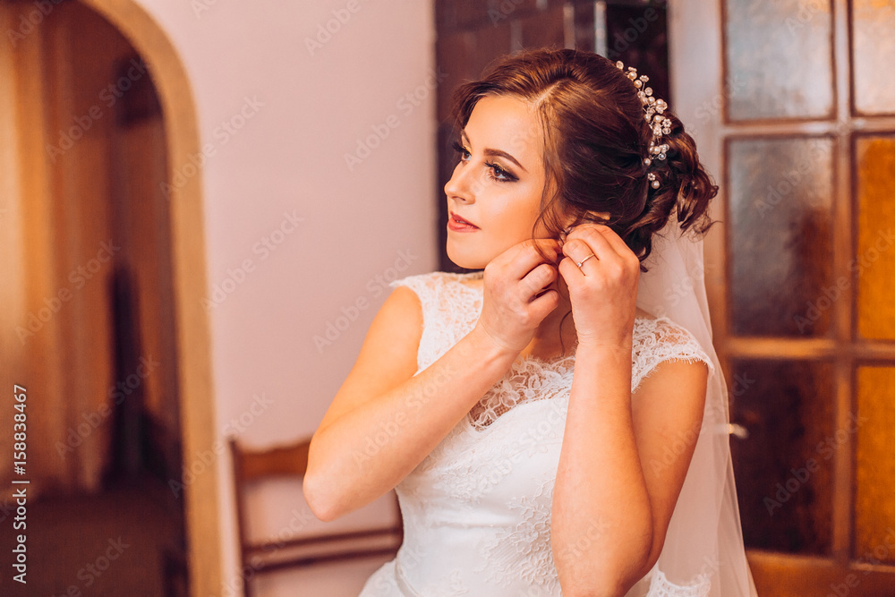 Portrait of beautiful bride. Morning of the bride. Wedding morning. Beautiful sexy lady in elegant white robe. Earrings on a female hand Portrait of beautiful bride. Morning of the bride. Wedding morning. Beautiful sexy lady in elegant white robe. Earrings on a female hand