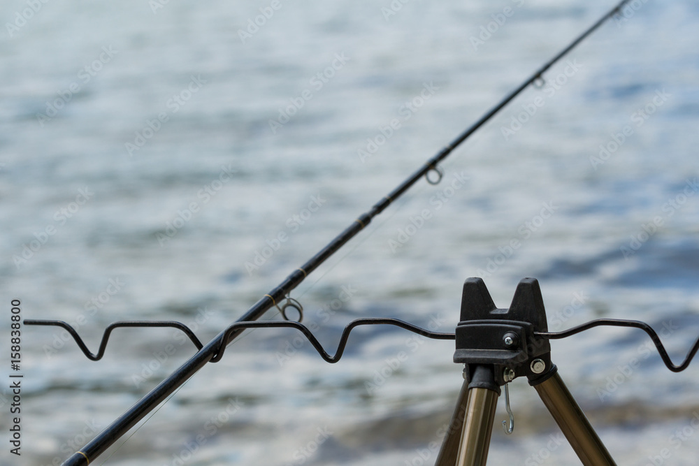 Obraz premium The fishing rod on the tripod in front of a river.