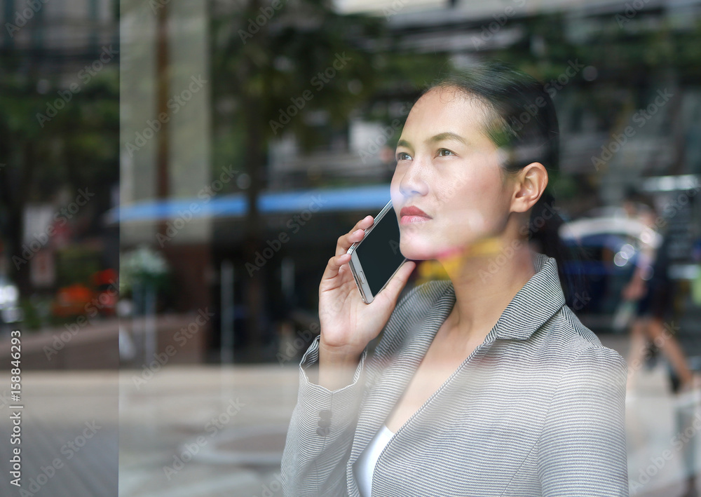 business woman using a smartphone at reflection glass of office building.
