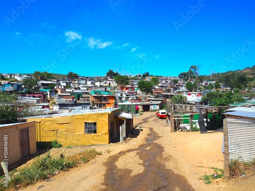Street of colorful informal settlements (Slum), huts made of metal in the Township or Cape Flats of Stellenbosch, Cape Town, South Africa with blue sky and clouds background