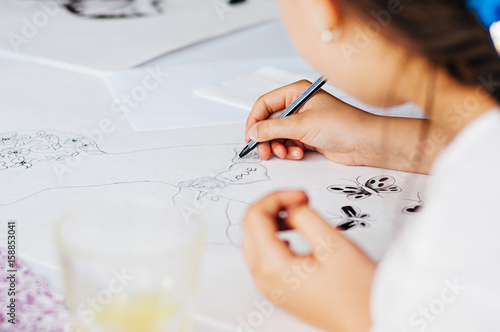 Unrecognizable little girl drawing a picture on paper. Close-up shot.