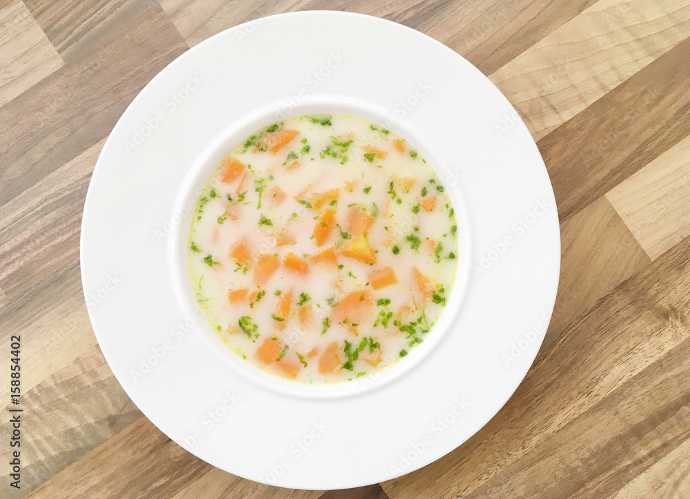 Vegetable carrot soup with cream and green herbs. Wooden background. Top view.