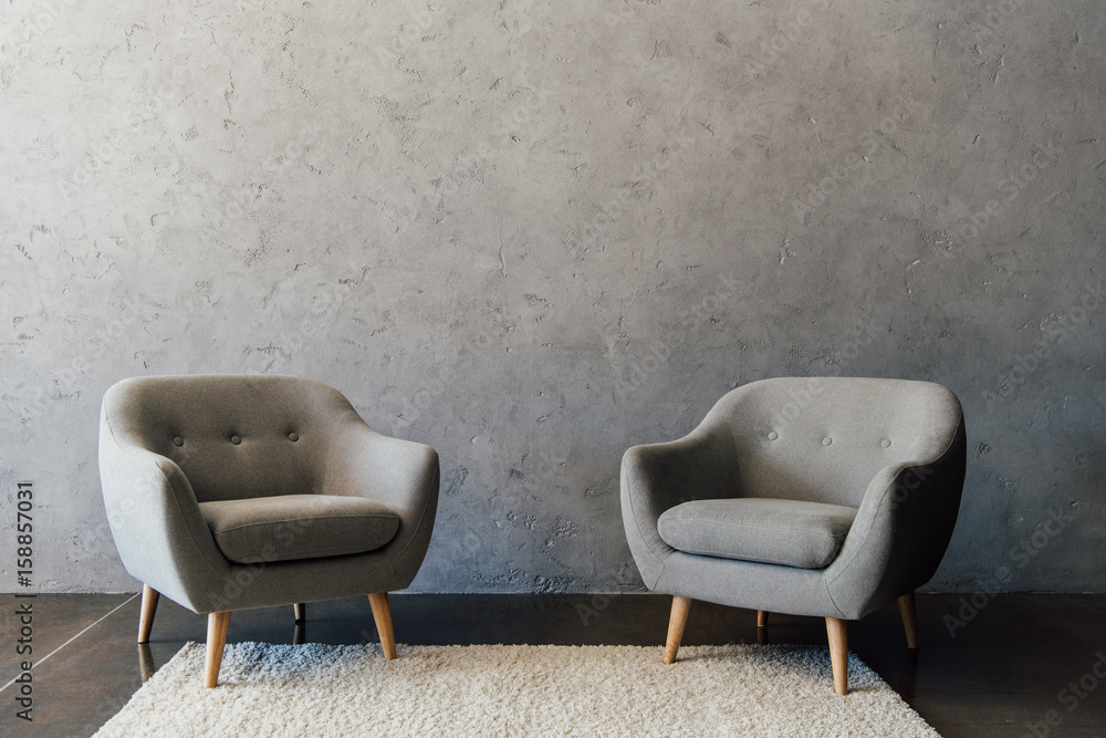 Two cozy grey armchairs standing on white carpet in empty room - obrazy, fototapety, plakaty 