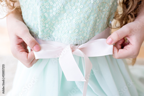 The girl knots a bow on a mint dress