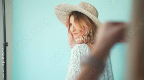 A pretty girl in a hat stands on a turquoise background, she is photographed. The photographer presses the shutter button and takes a picture of the young girl. Backstage of photosession photo