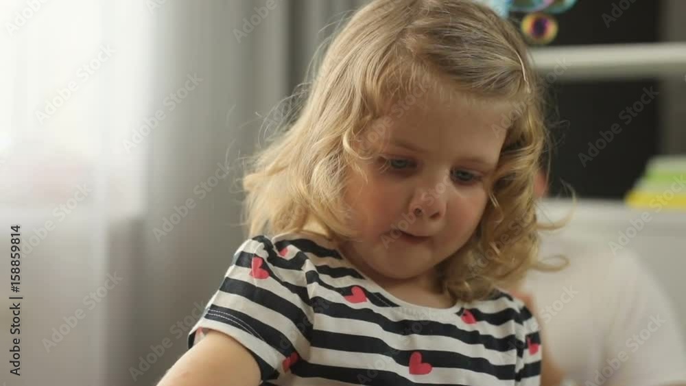 Portrait of pretty little girl with blond curly hair and blue eyes in home playing with bubble blower. Indoor. Portrait of pretty little girl with blond curly hair and blue eyes in home playing with bubble blower. Indoor.