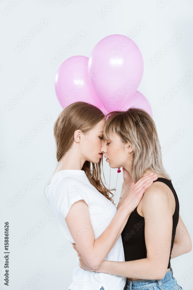 Beautiful young lesbian couple holding pink balloons and kissing