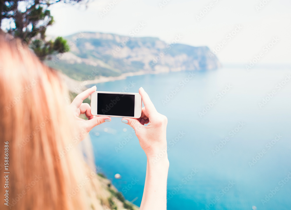 Young smiling woman taking travel photo on trekking excursion day - Hipster girl taking photo at view point with blue ocean background - Concept of healthy lifestyle in beauty of nature