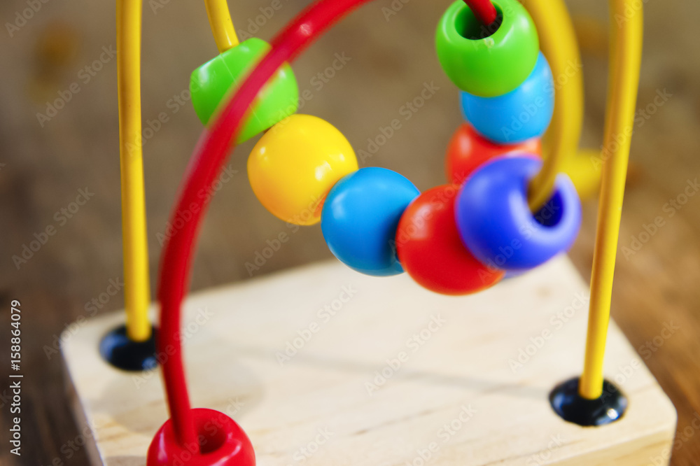 A child's bead roller coaster toy in primary colors over wooden background