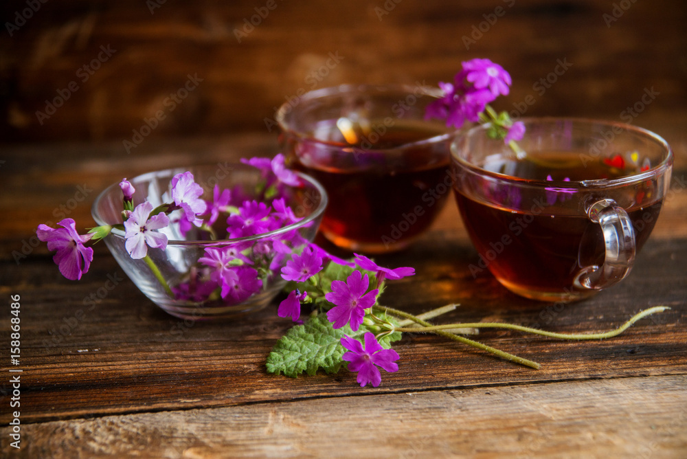 Glass cup of tea on old wooden surface. Small white flowers. Glass cup of tea on old wooden surface. Small white flowers.