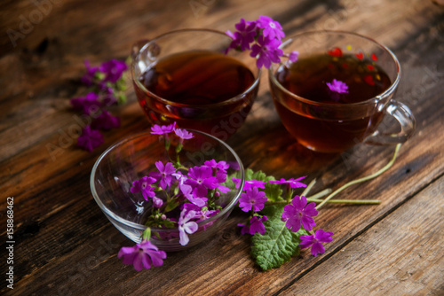 Glass cup of tea on old wooden surface. Small white flowers.