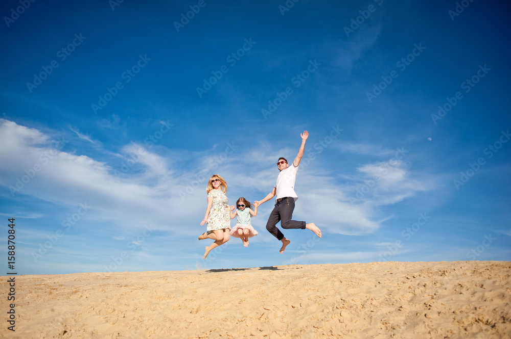 Beautiful happy family walking, running, jumping, having fun along the sand on the beach against the background blue sky in summer vacation Beautiful happy family walking, running, jumping, having fun along the sand on the beach against the background blue sky in summer vacation