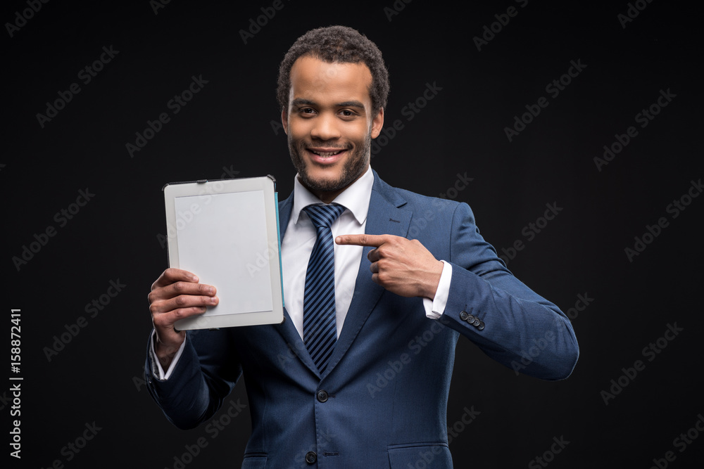 Portrait of successful businessman pointing on digital tablet isolated on black Portrait of successful businessman pointing on digital tablet isolated on black
