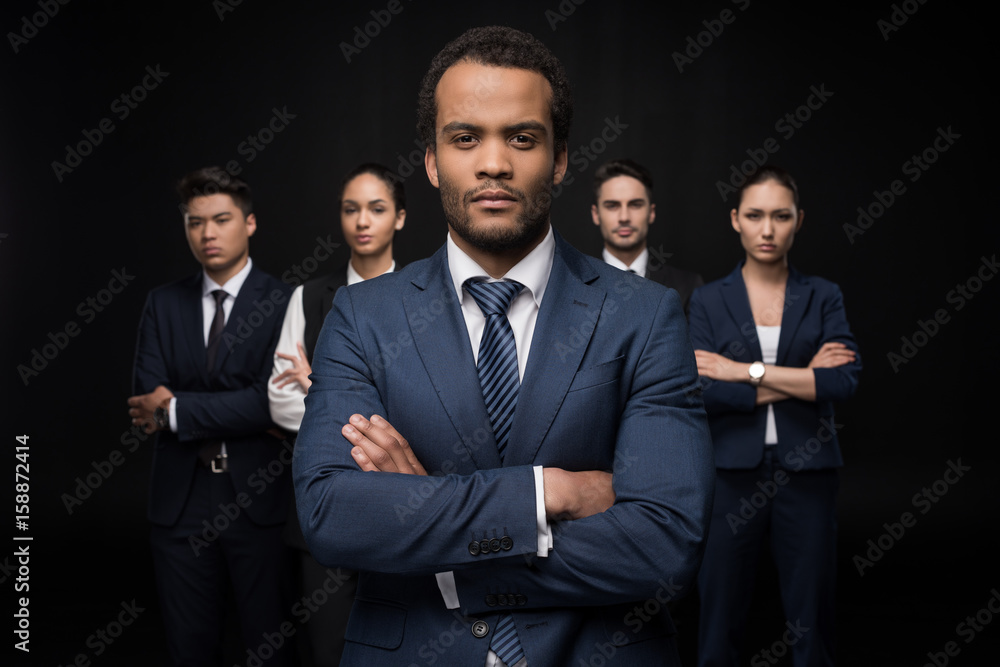 Serious businessman with his business colleagues standing with arms crossed and looking at camera isolated on black Serious businessman with his business colleagues standing with arms crossed and looking at camera isolated on black