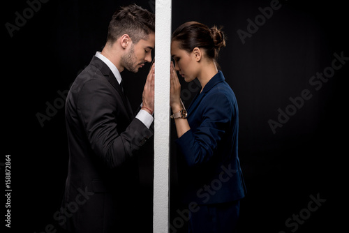 Side view of sad couple in formal wear separated by wall isolated on black