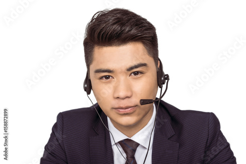 Smiling young asian call center operator in headset looking at camera