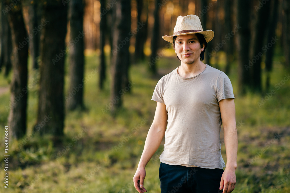Young and lonely native american indian latino indigenous man standing in forest outdoor in summer in straw hat, casual clothing above bonfire with smoke on vacation. Evening sunset. Weekend. Young and lonely native american indian latino indigenous man standing in forest outdoor in summer in straw hat, casual clothing above bonfire with smoke on vacation. Evening sunset. Weekend.