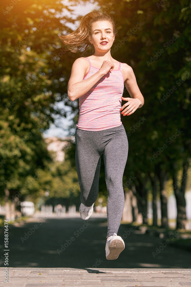 Pretty sporty woman jogging at park in sunrise light Pretty sporty woman jogging at park in sunrise light