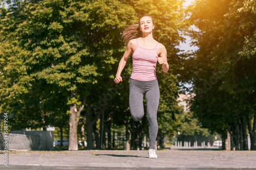 Pretty sporty woman jogging at park in sunrise light