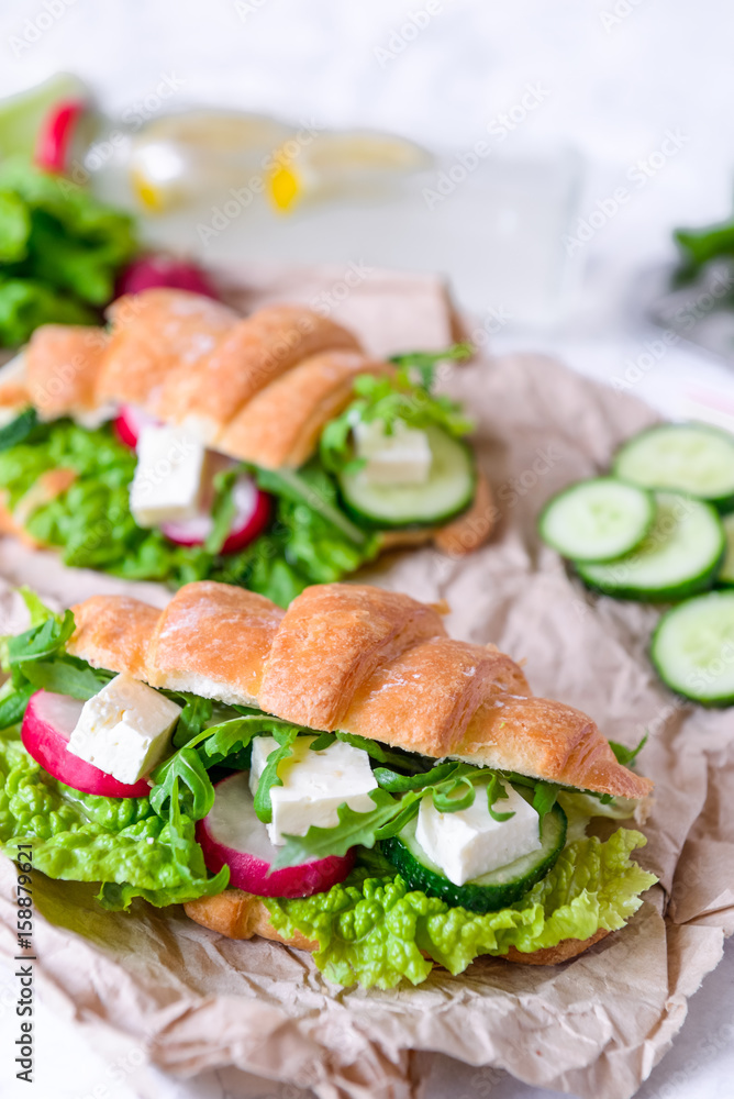 Croissant sandwich with cheese and vegetables for healthy snack, craft paper and greens background. Picnic summer food. Selective soft focus