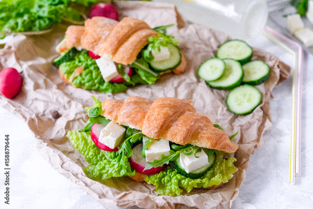 Croissant sandwich with cheese and vegetables for healthy snack, craft paper and greens background. Picnic summer food. Selective soft focus