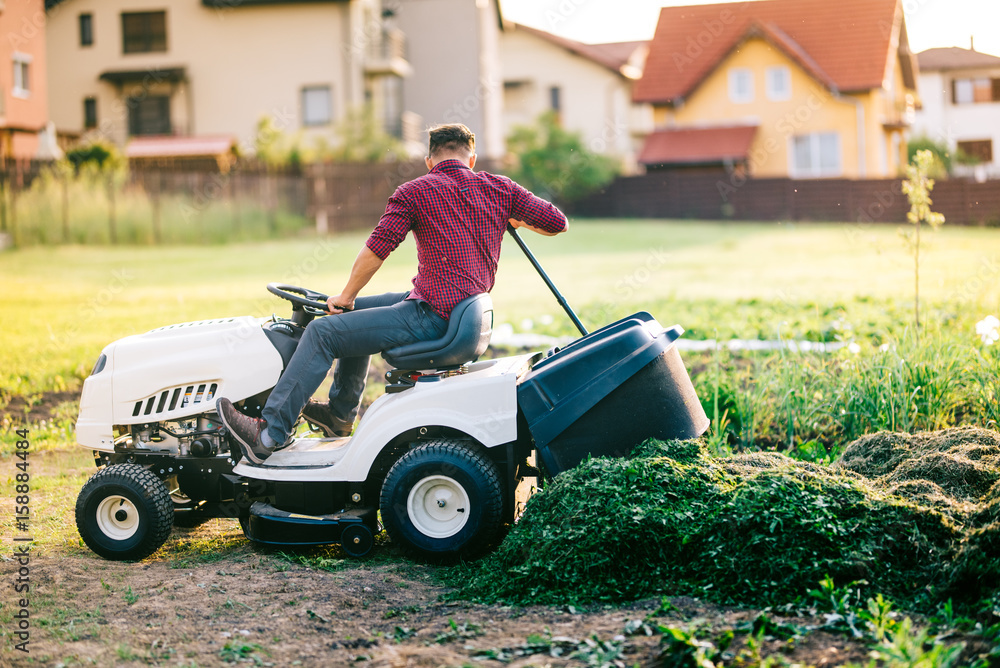 Man with lawn tractor unloading cut grass during landscaping works Man with lawn tractor unloading cut grass during landscaping works
