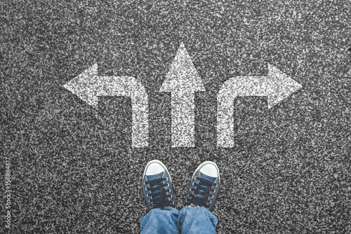 Sneakers on the asphalt road with three arrows pointing. Making decisions concept