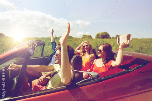 happy friends driving in cabriolet car at country