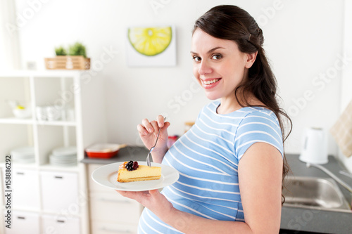 happy pregnant woman eating cake at home kitchen
