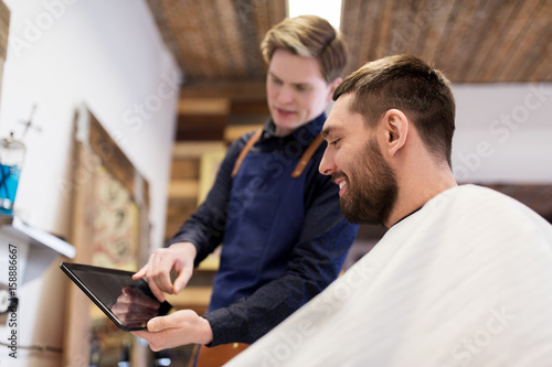 barber showing tablet pc to man at barbershop