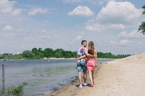 Young couple hugging and smiling at each other on the river bank. Walking along the sandy beach