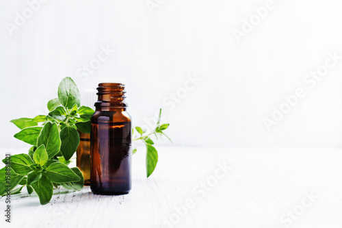 Essential oil of oregano in dark bottles, fresh green mint on white wooden background, selective focus .