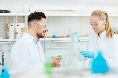 Portrait of two scientists, man and woman, working with test tubes in modern laboratory, studying reactant liquids